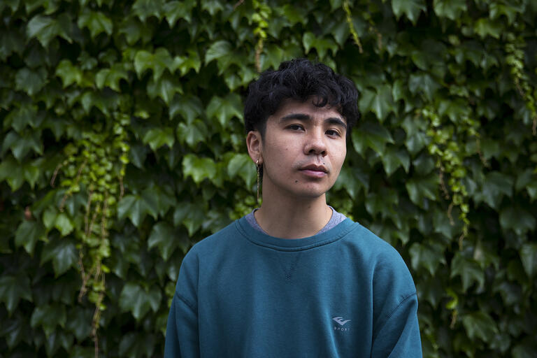 Person in a teal sweatshirt standing in front of a wall covered with green ivy.