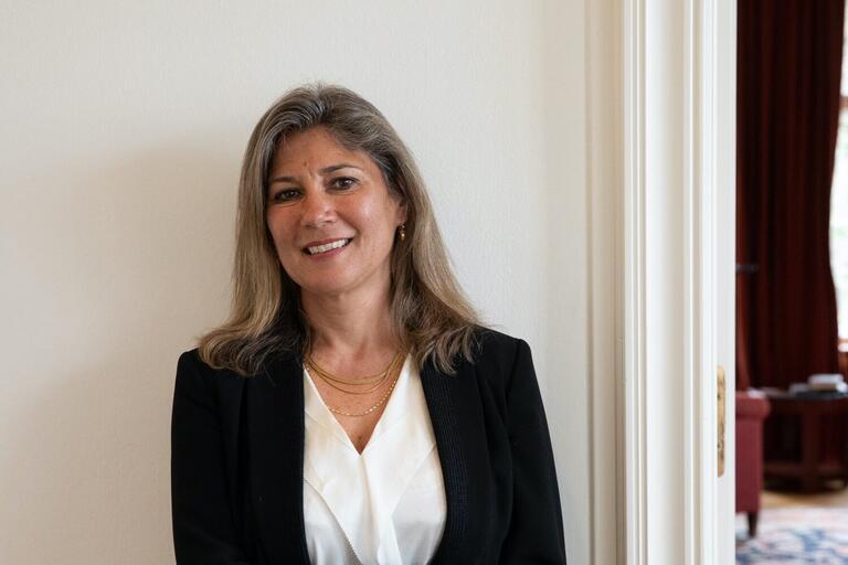 Professional woman with greyish hair and a black blazer standing near a doorway, smiling.