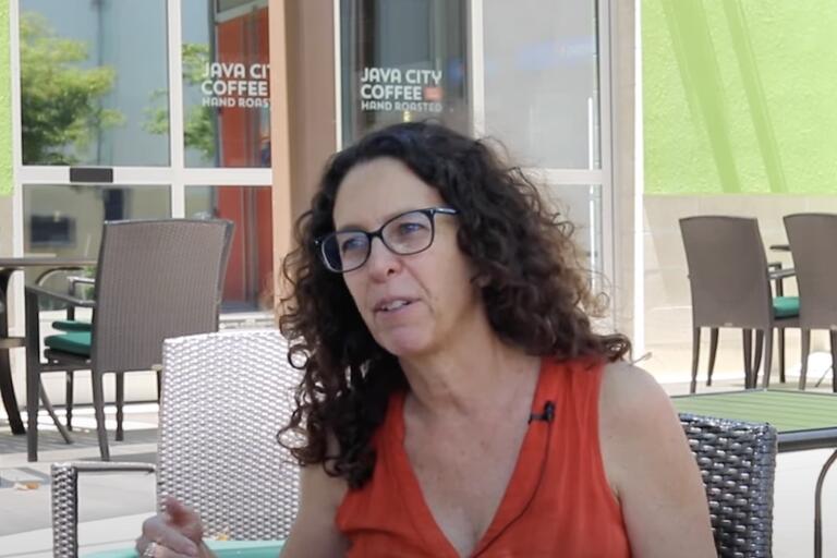 Woman with curly hair and glasses sitting at an outdoor café.