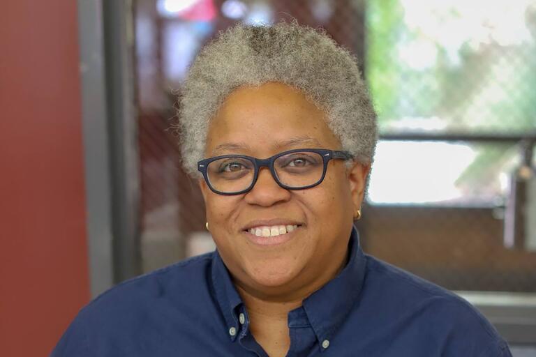 Close-up portrait of a person with short gray hair, glasses, and a navy-blue shirt, smiling.