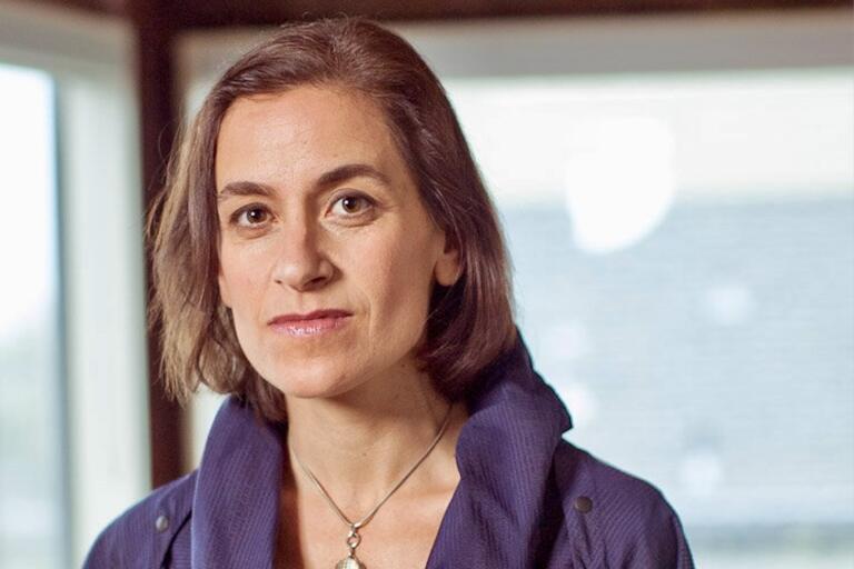 Portrait of a person with medium-length brown hair wearing a blue jacket and a pendant necklace.