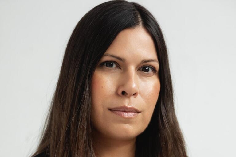 Close-up portrait of a person with long dark brown hair and a neutral expression against a plain light background.