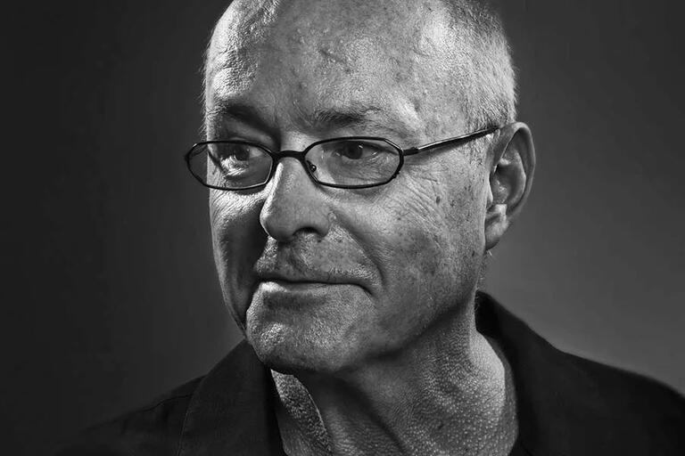 Grayscale close-up portrait of a man with glasses looking to the left.