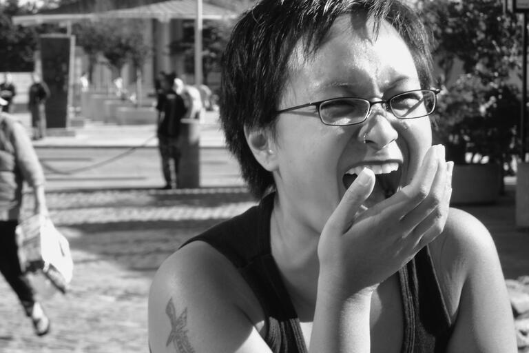 Person laughing and covering their mouth in a black-and-white photograph with a busy outdoor backdrop.
