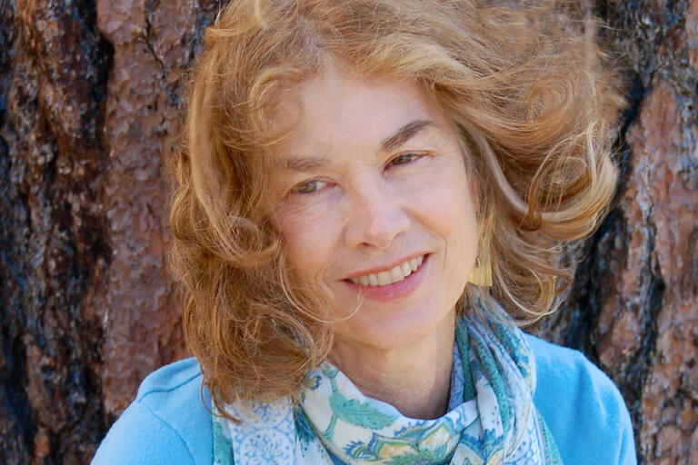 Smiling woman with light brown, wavy hair in front of a large tree trunk.
