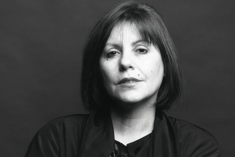 Black-and-white portrait of a woman with short dark hair, wearing a dark top and jacket, with a neutral expression.