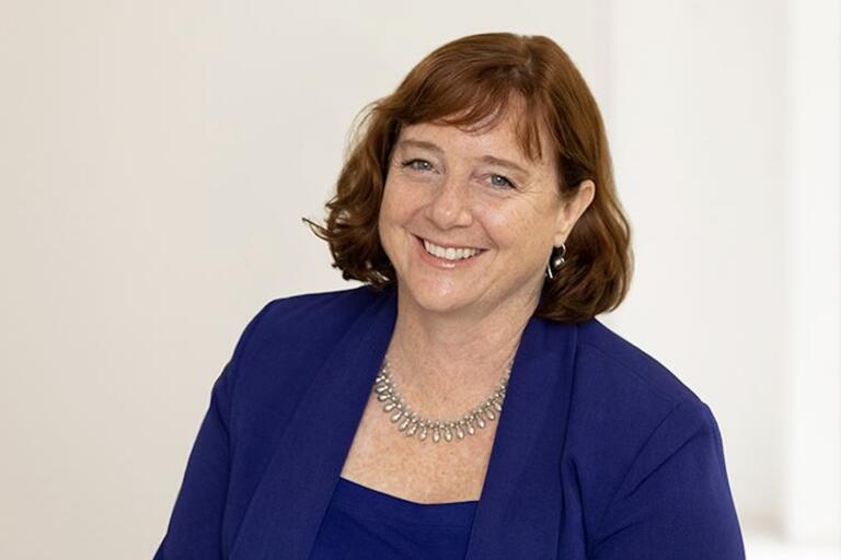 Smiling person with reddish-brown hair wearing a blue blazer.