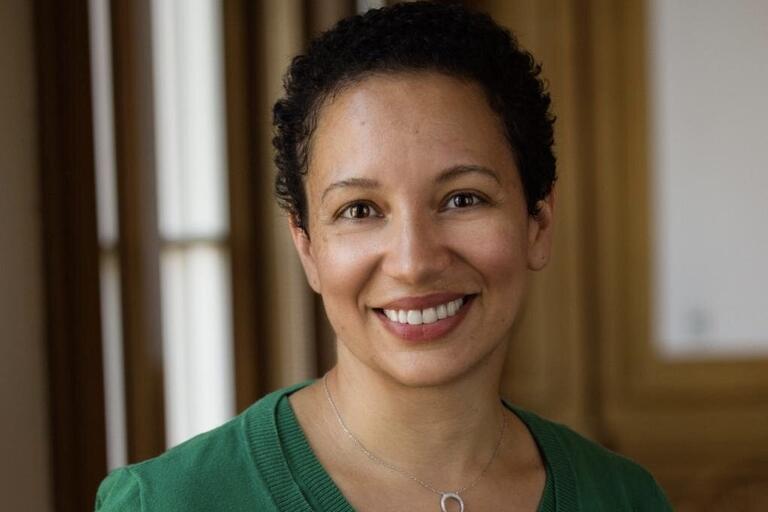 Person with short curly hair smiling, wearing a green top and a crescent-shaped necklace.