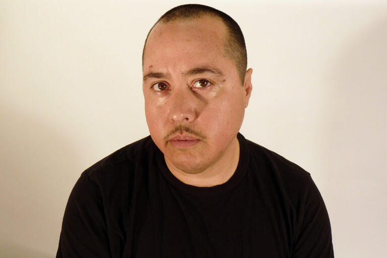 Portrait of a person with short hair, a mustache, and a black T-shirt against a plain white background.