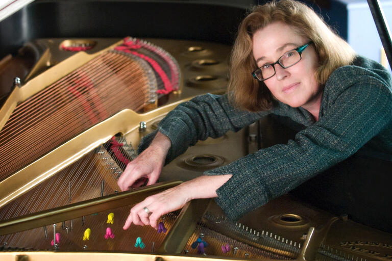 Person leaning inside a grand piano, arranging colorful felt pieces among the strings.