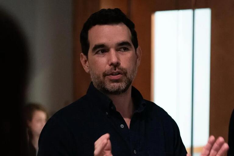 Man with short black hair and trimmed beard speaking indoors.