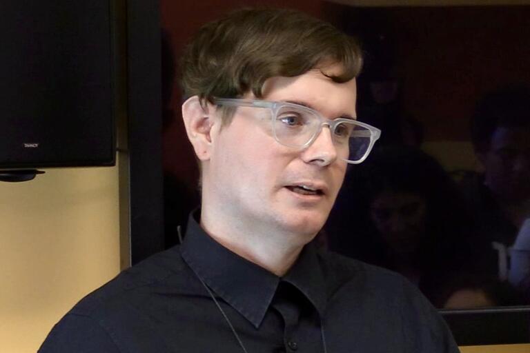 Person with clear-framed glasses and side-parted hair, wearing a dark blue shirt.