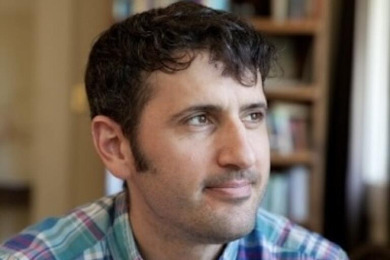 Close-up photo of a person wearing a plaid shirt, with bookshelves in the background.