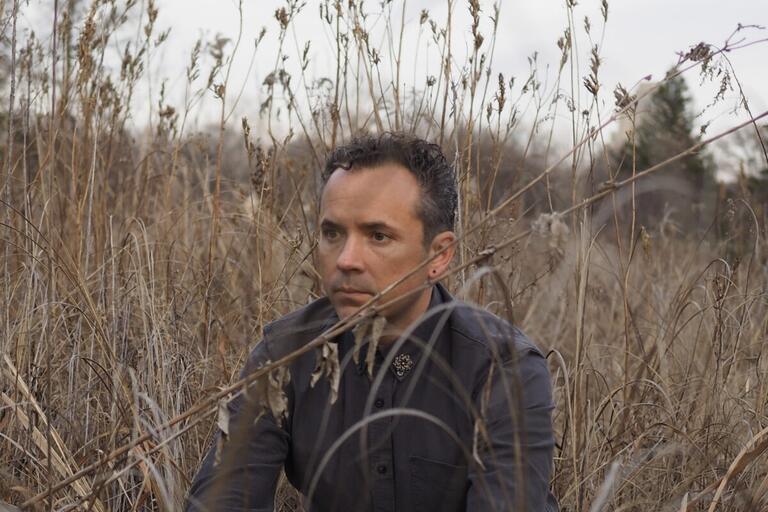 Person sitting in tall, dry grasses, looking to the left.