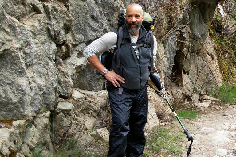 Man hiking on a rocky trail with a large backpack and walking stick.