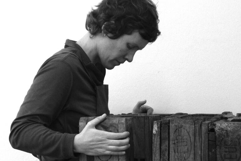 A person in an apron focusing on a wooden structure.