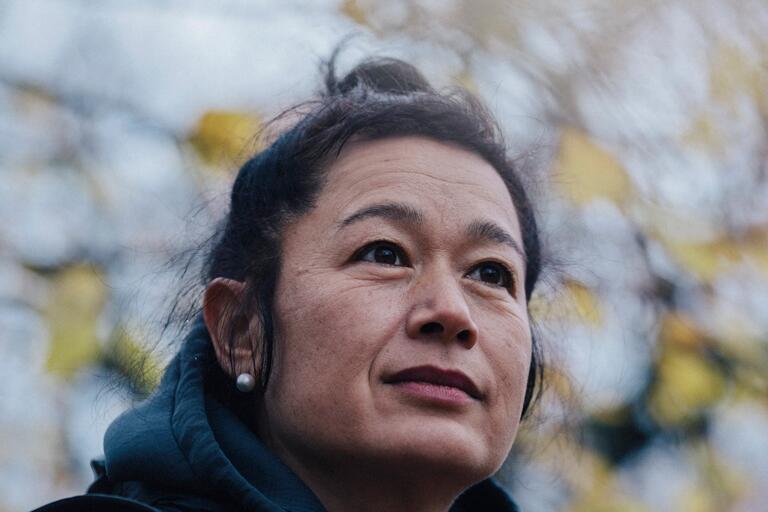 Close-up portrait of a woman looking upward with a thoughtful expression against a blurred, leafy background.