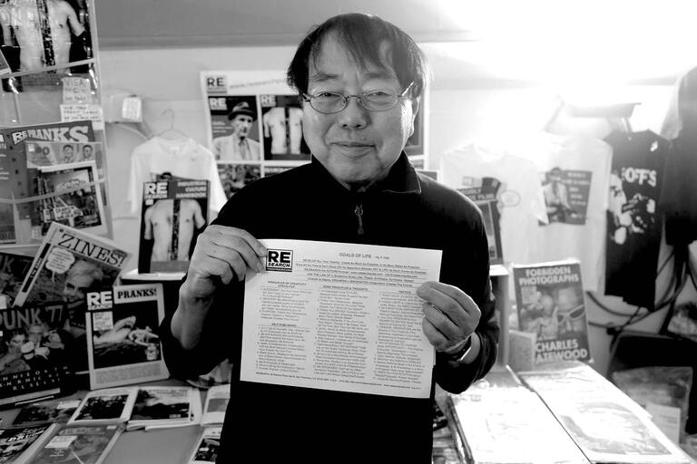 A man holding a document with the heading "GOALS OF LIFE" in a bookstore setting.
