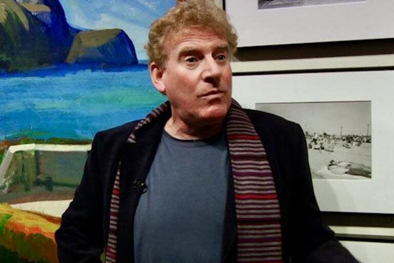 Man in front of a colorful painting and black and white photographs.