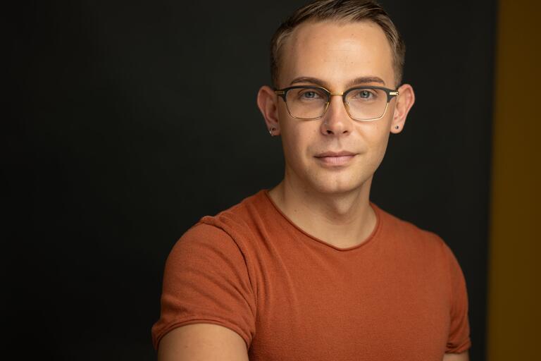 Portrait of a person in glasses and an orange shirt against a dark background.
