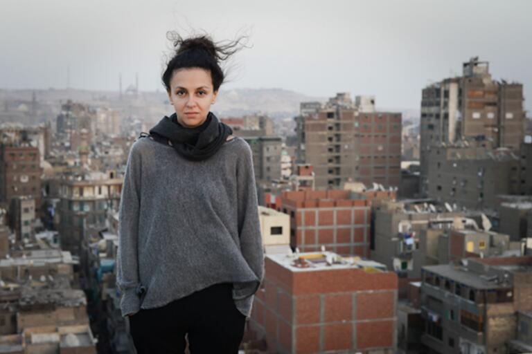 Woman standing on a rooftop with a cityscape in the background.