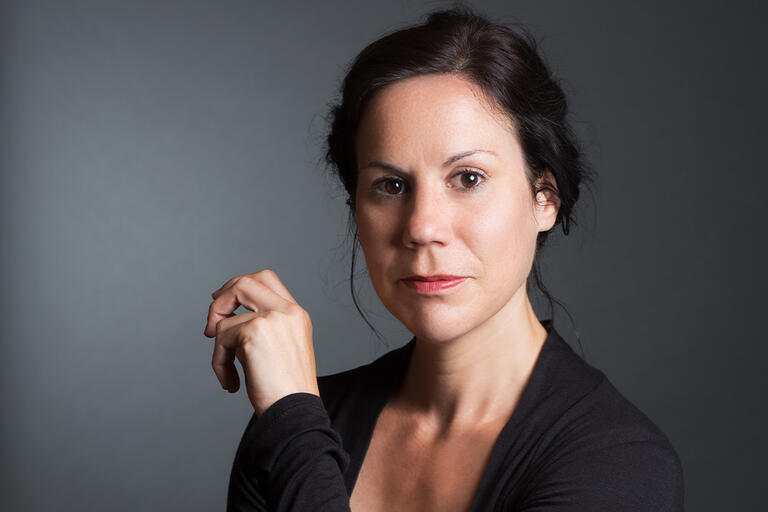 Portrait of a person with dark hair and a black top against a gray background.