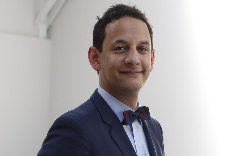 Portrait of a man in a suit and bow tie, standing against a light background.