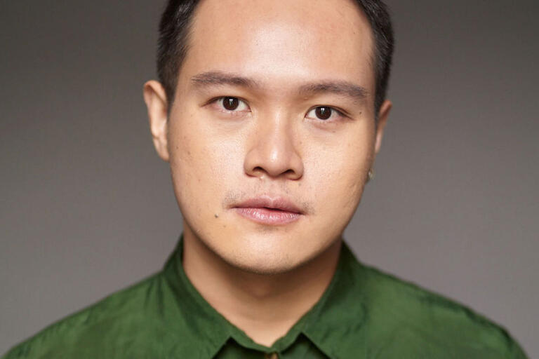 Portrait of a person with short, dark hair wearing a green shirt against a grey background.