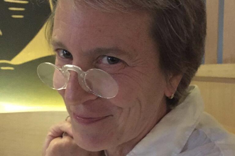 Close-up of a person wearing small, round glasses, looking directly at the camera with a playful expression.