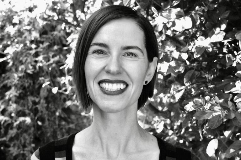 Black-and-white portrait of a smiling woman with short hair in front of foliage.