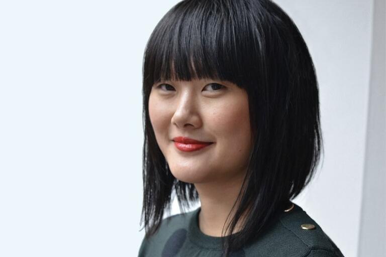 Person with shoulder-length black hair and a blunt fringe, wearing a dark green top with polka dots and gold buttons.