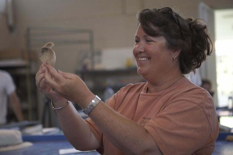 Woman smiling while holding a small ceramic artifact indoors.