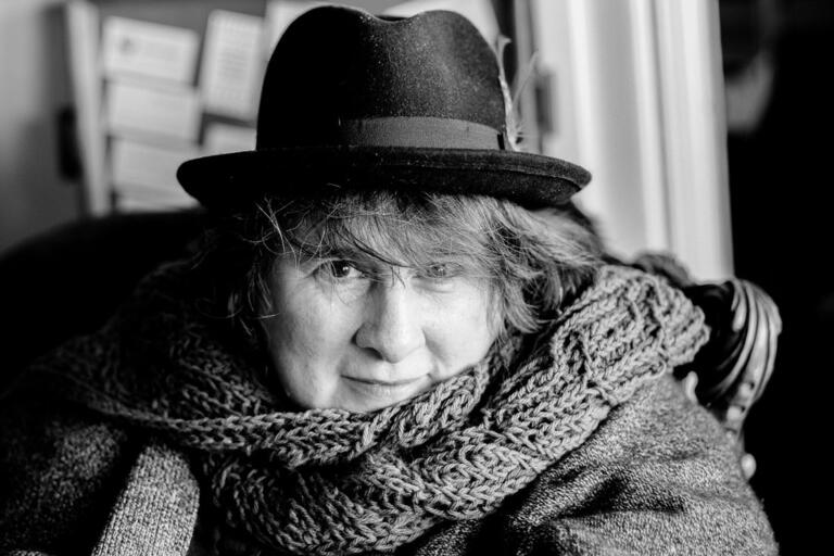 Black-and-white portrait of a person wearing a dark hat and a chunky-knit scarf.