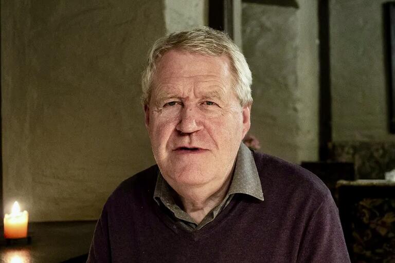 Older man indoors with a lit candle in the background.