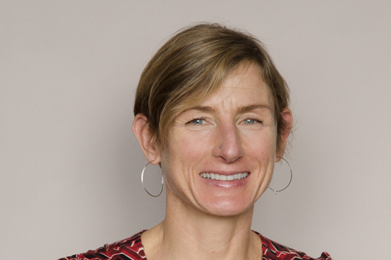 Headshot of a person smiling with short light brown hair and wearing hoop earrings.