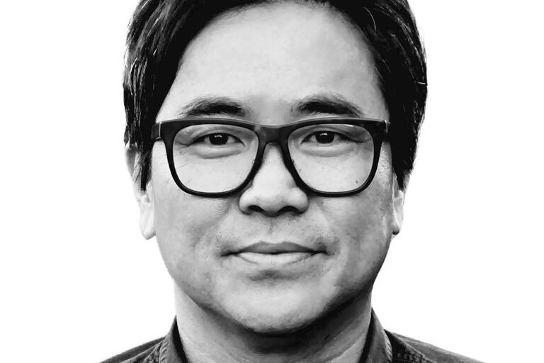 Black and white portrait of a person with short, dark hair, wearing rectangular glasses and a dark button-up shirt.