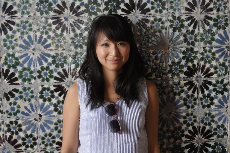 Woman standing in front of a patterned tiled wall with geometric designs.