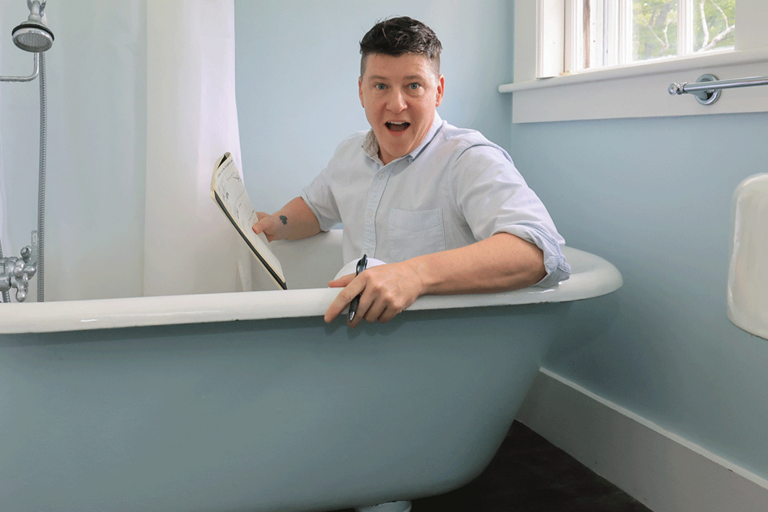 Person sitting in a clawfoot bathtub with a clipboard, in a light blue bathroom.