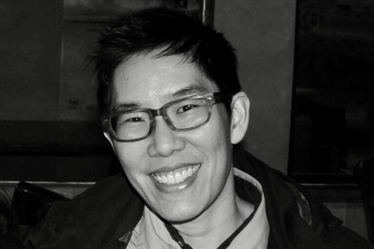 Black-and-white close-up of a person with glasses smiling.