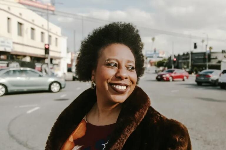 Person smiling at an intersection with buildings and cars in the background.