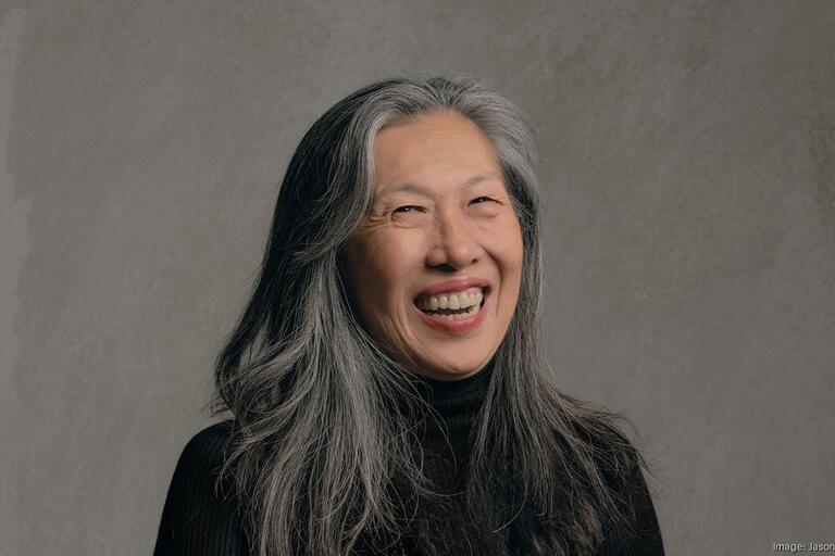 Smiling person with long gray hair against a light gray background.