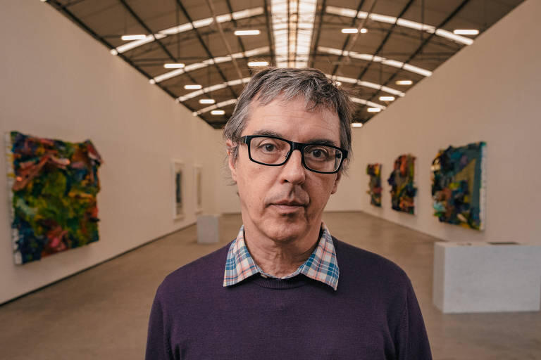 Person with graying hair and glasses in a modern art gallery with colorful abstract artworks on the walls.