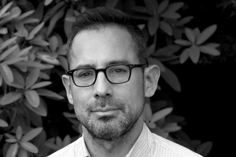Black-and-white portrait of a man wearing glasses with a foliage background.