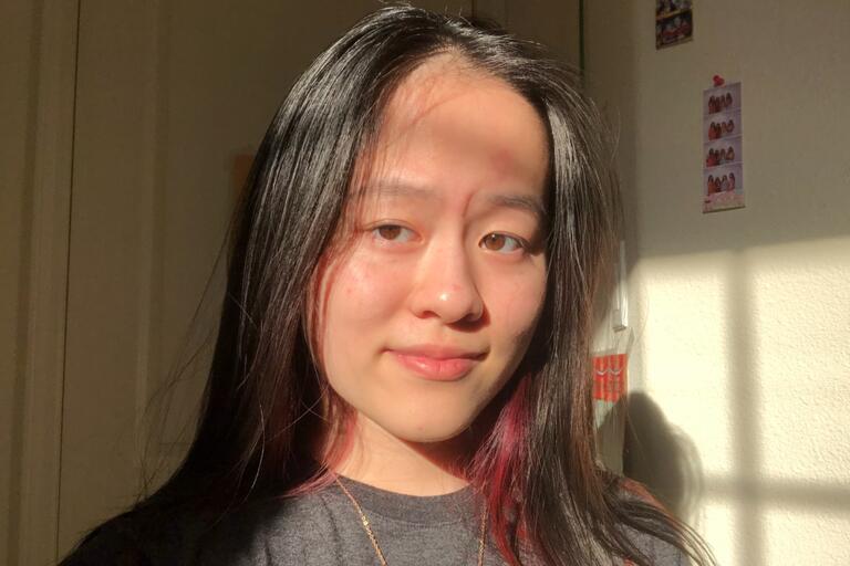 Close-up of a person with long dark hair in sunlight, casting shadows on their face.