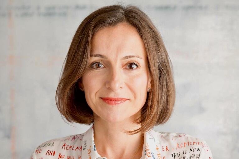 : Close-up of a woman with straight brown hair wearing a white shirt with colorful handwritten text.