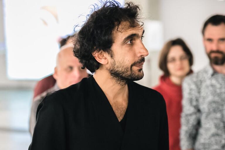 Man with a cane standing in a group indoors.