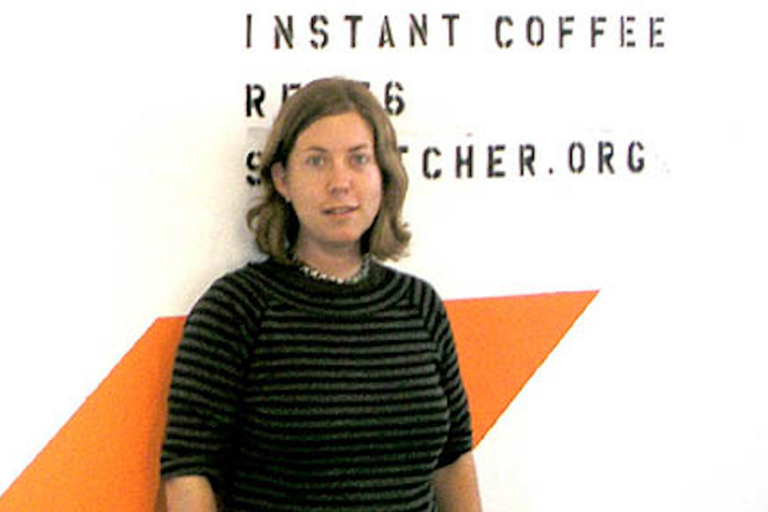 Person wearing a dark-striped shirt stands against a white wall with text and an orange triangular shape.