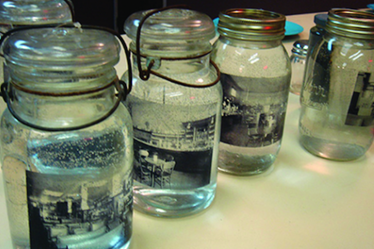 Several mason jars filled with water and old-fashioned photographs, each with different closures, displayed on a white surface.