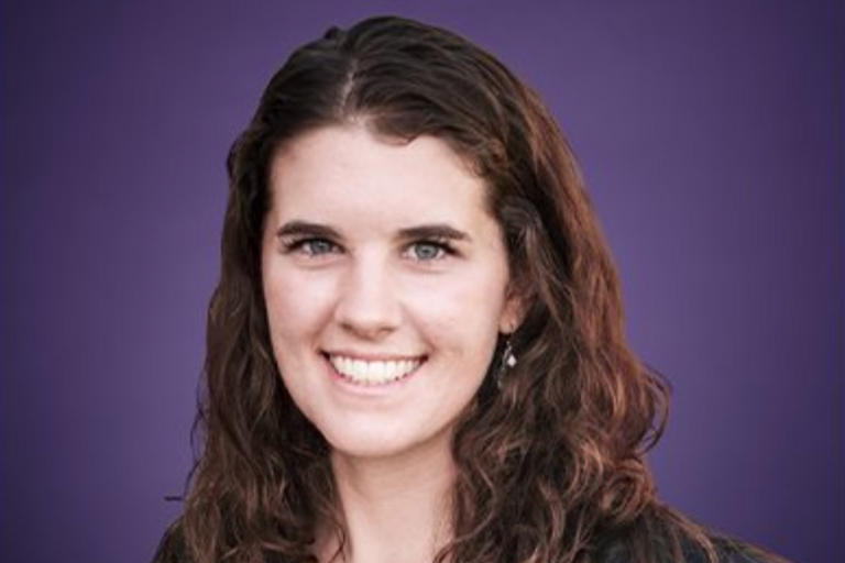 Portrait of a person with wavy brown hair against a purple background.