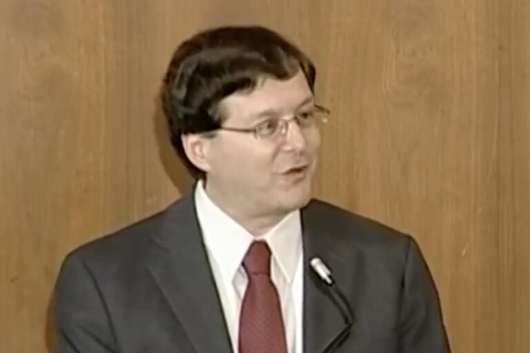 Man in a suit speaking at a podium.